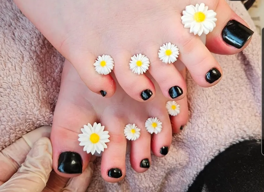 Fertige Pediküre mit schwarzem Shellac und Gänseblümchen-Zehentrennern auf rosa Handtuch